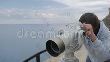 十五岁的男孩穿着灰色连帽衫，从高高的观景台上望着大海<strong>进</strong>入望远镜。